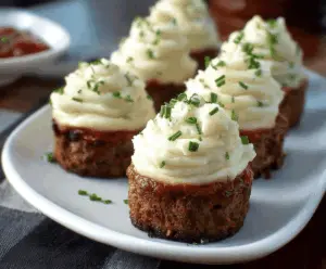 Delicious meatloaf cupcakes topped with creamy mashed potato frosting on a plate.