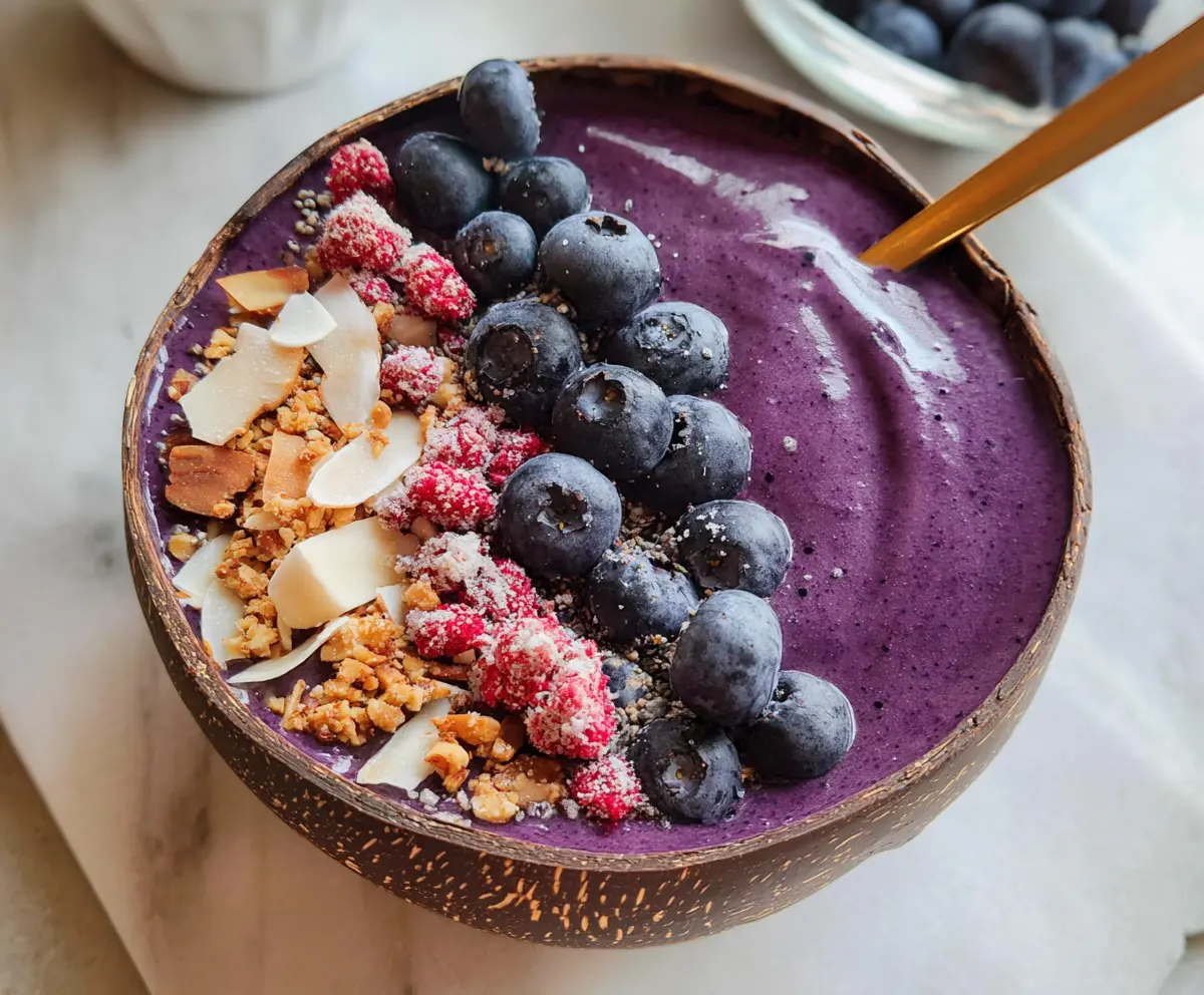 Fresh blueberry smoothie bowl topped with colorful fruits and granola, showcasing a healthy breakfast option.