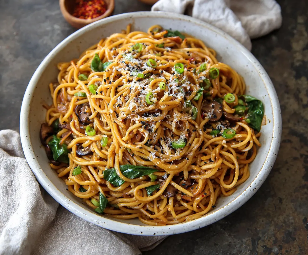 Delicious Asian garlic noodles garnished with green onions and sesame seeds on a white plate.