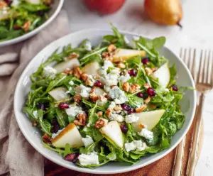 Fresh arugula and ripe pear salad with walnuts and feta cheese on a white plate.