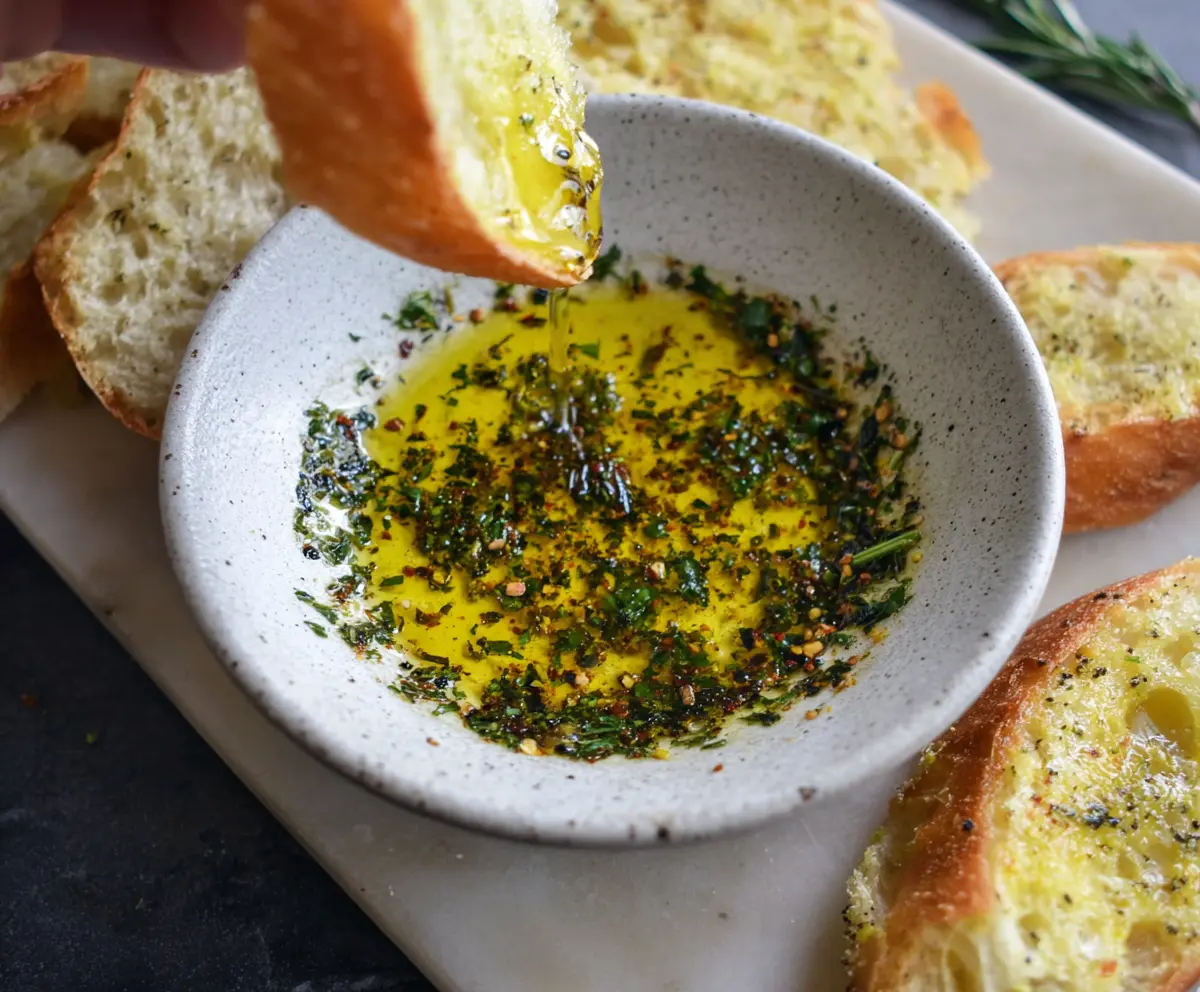 Delicious olive oil bread dip served with fresh herbs and crusty bread for dipping.
