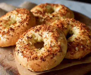 Delicious homemade onion bagels with a shiny golden crust served on a wooden board.