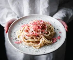 Creamy Pink Cacio E Pepe pasta dish garnished with herbs on a rustic plate.