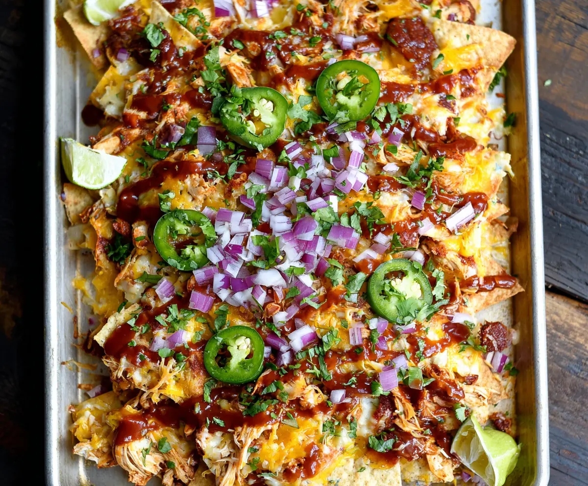 Delicious Sheet Pan BBQ Chicken Nachos topped with melted cheese, jalapenos, and fresh cilantro on a baking sheet.