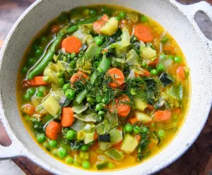 Fresh spring vegetable soup with vibrant seasonal vegetables in a bowl on a rustic wooden table.