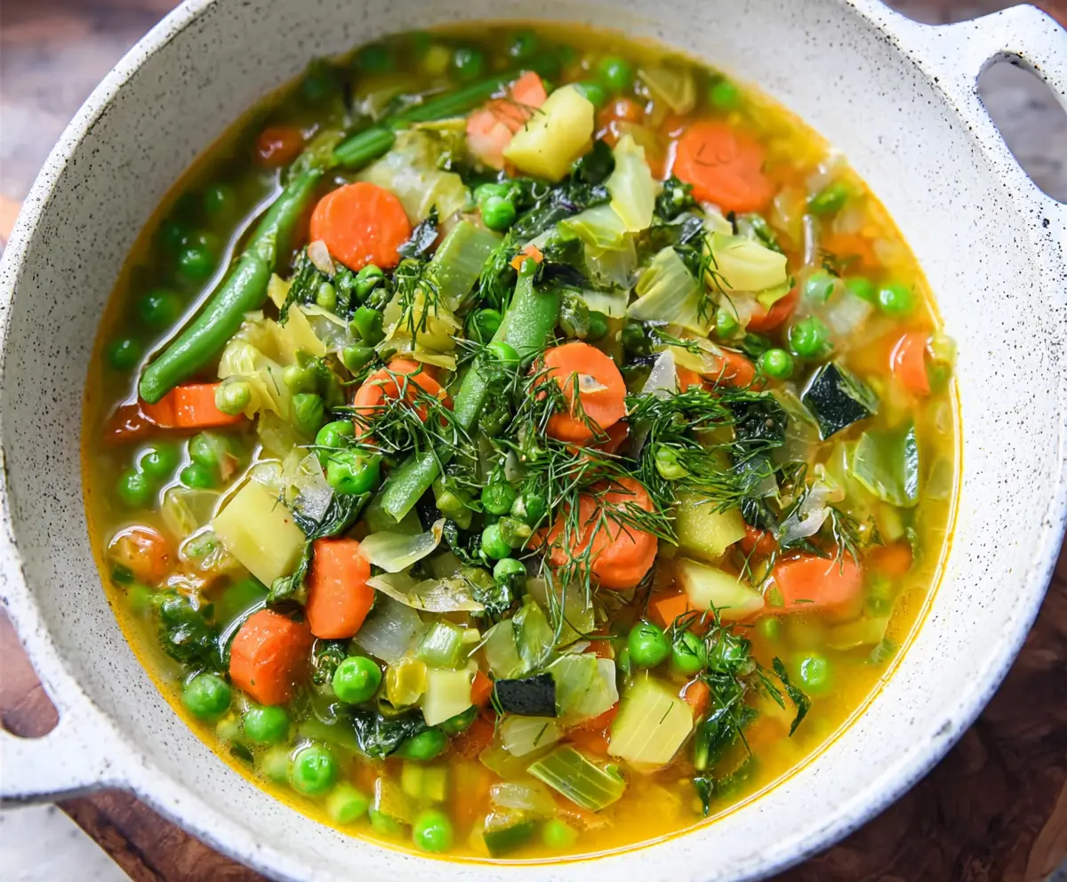 Fresh spring vegetable soup with vibrant seasonal vegetables in a bowl on a rustic wooden table.